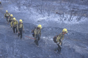Firefighters walk over charred terrain