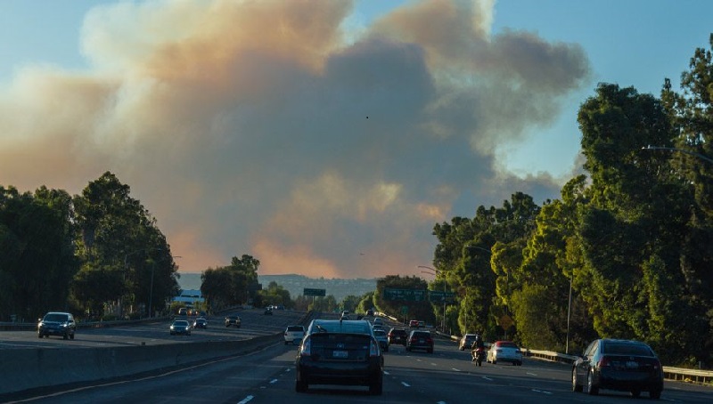 Cars on California freeway with view of wildfire in background