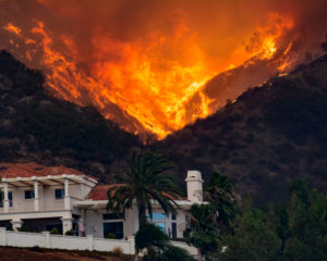 A wildfire burns the hillside behind a California home