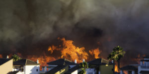 A wildfire burns near a row of houses.