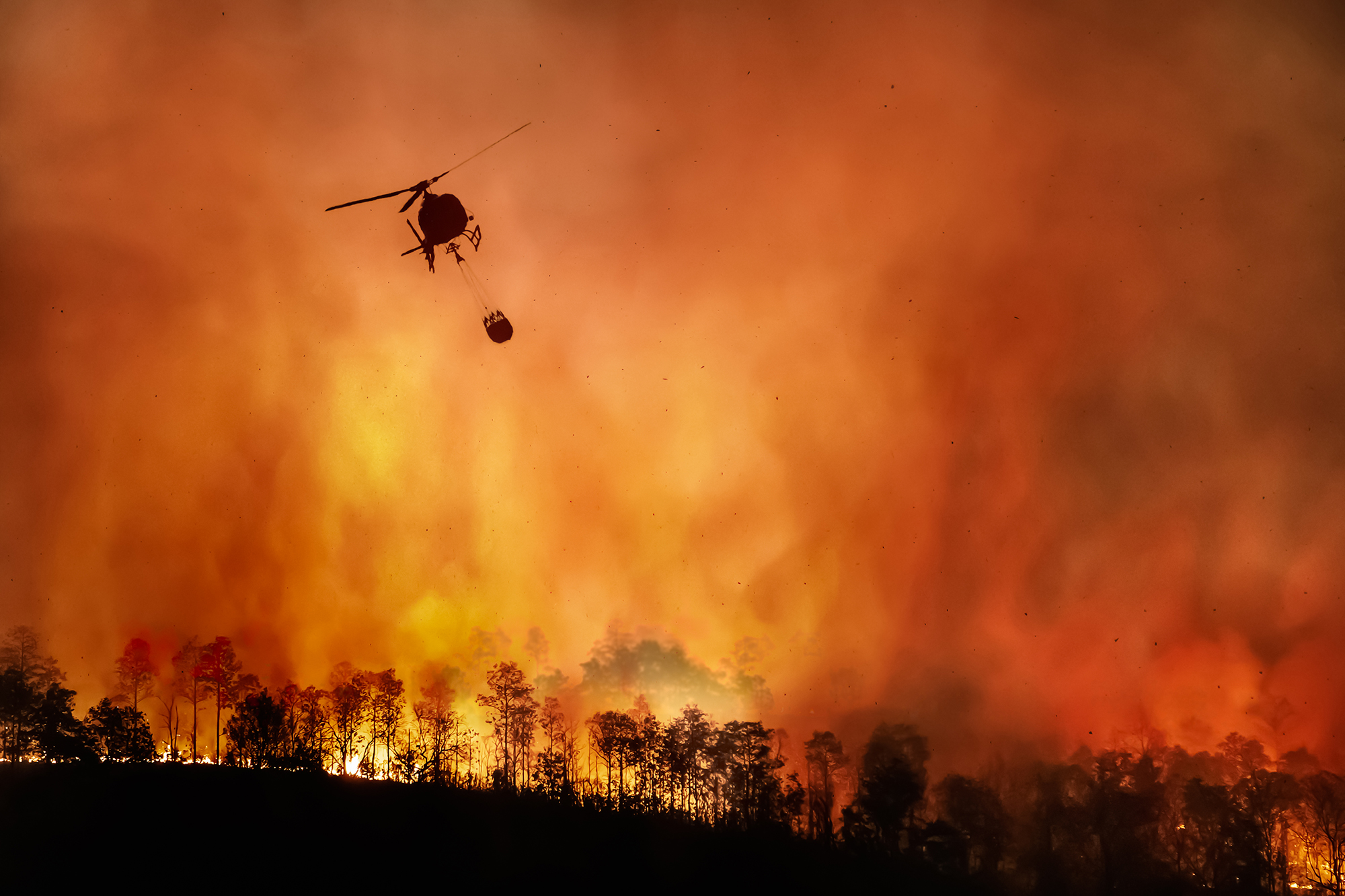 A helicopter makes a water drop fighting a wildfire.