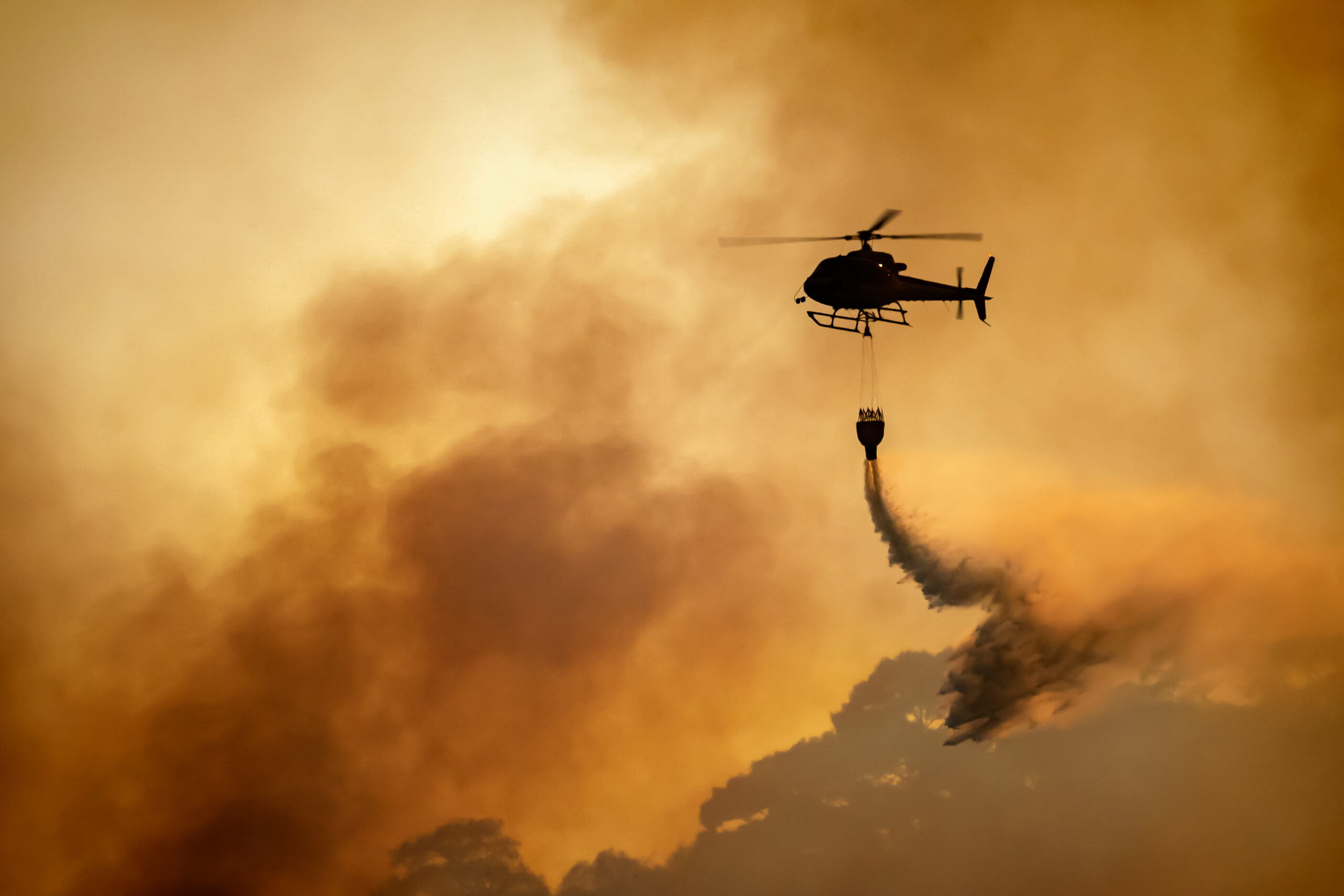 A helicopter drops water on a wildfire.