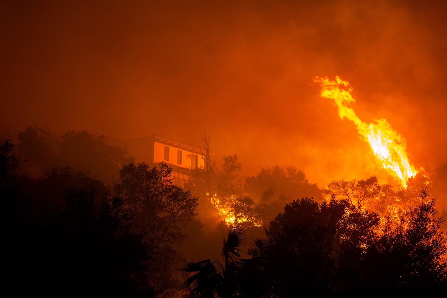 A wildfire threatens a home in Los Angeles County, highlighting California's deepening home insurance crisis.